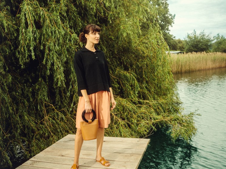 Woman in black pullover and coral shorts with yellow bag standing on wooden dock by water