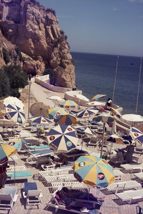 Beach scene with colorful umbrellas, lounge chairs and people at a Mediterranean coastal resort