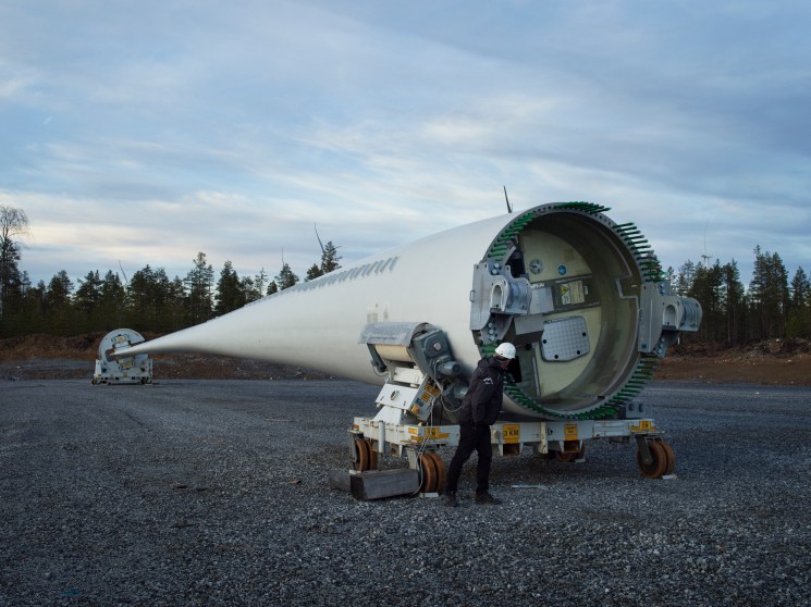 Worker inspecting a massive wind turbine nacelle on the ground.