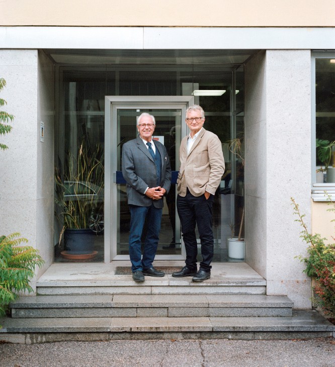 Two men in business attire standing in a modern glass-fronted building entrance