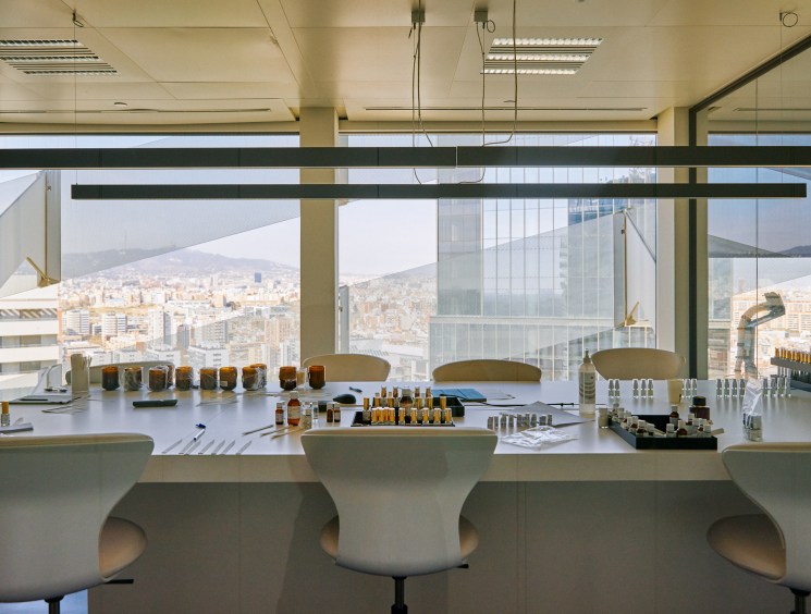 Modern perfumery lab with white tables, bottles, testing equipment and city views through floor-to-ceiling windows