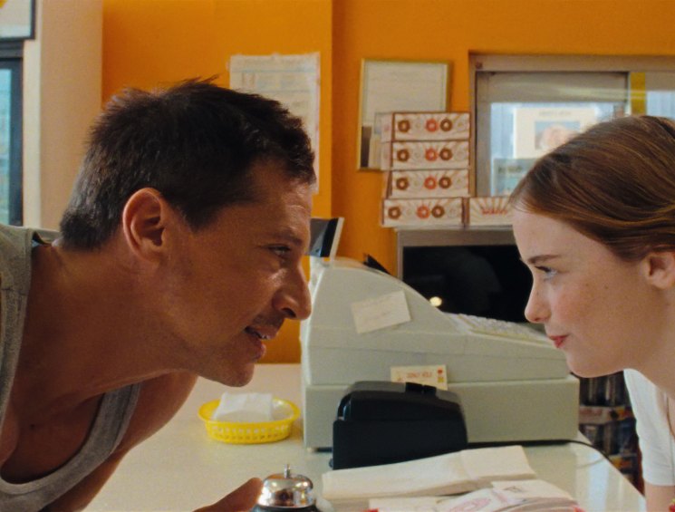 A man in a tank top and woman in white clothing lean toward each other looking at a microscope in a laboratory setting