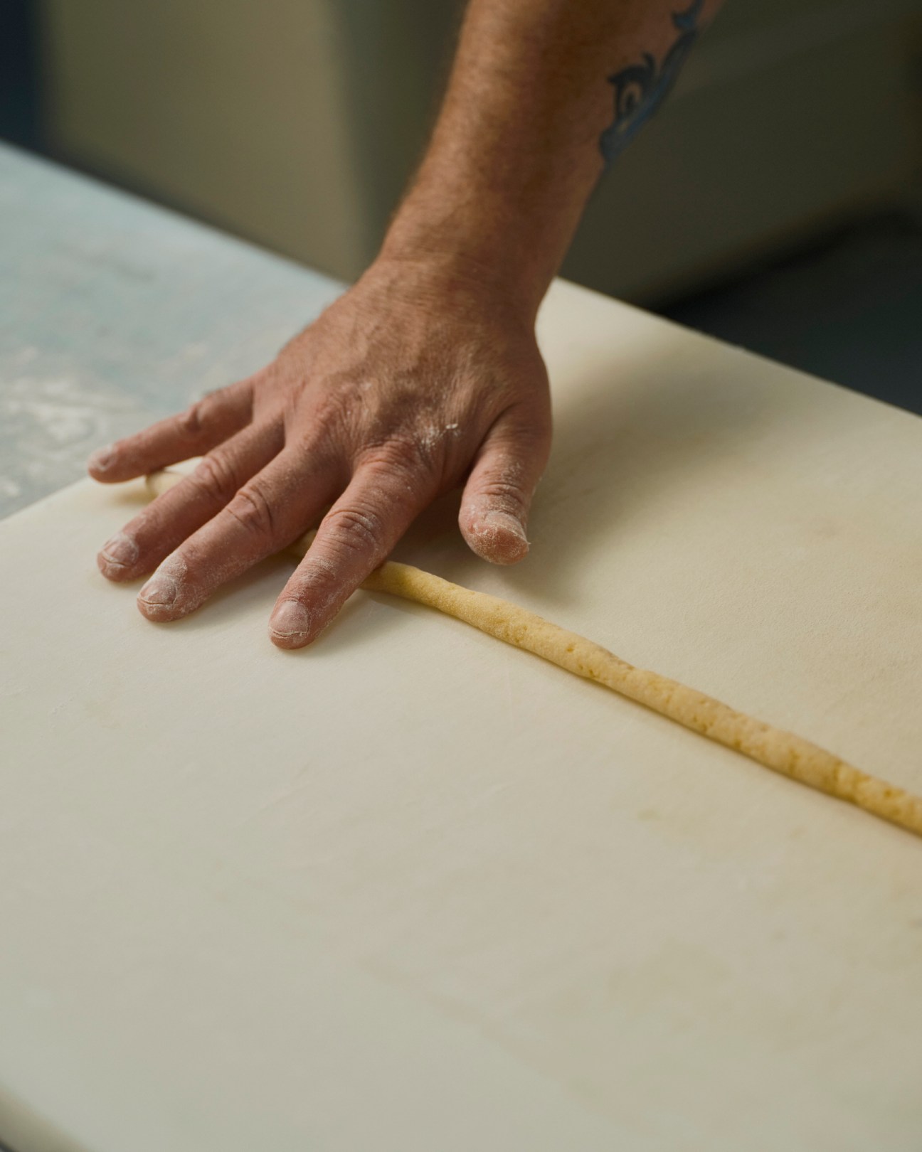 Flour-dusted hands rolling traditional dough on white surface in artisanal bakery kitchen