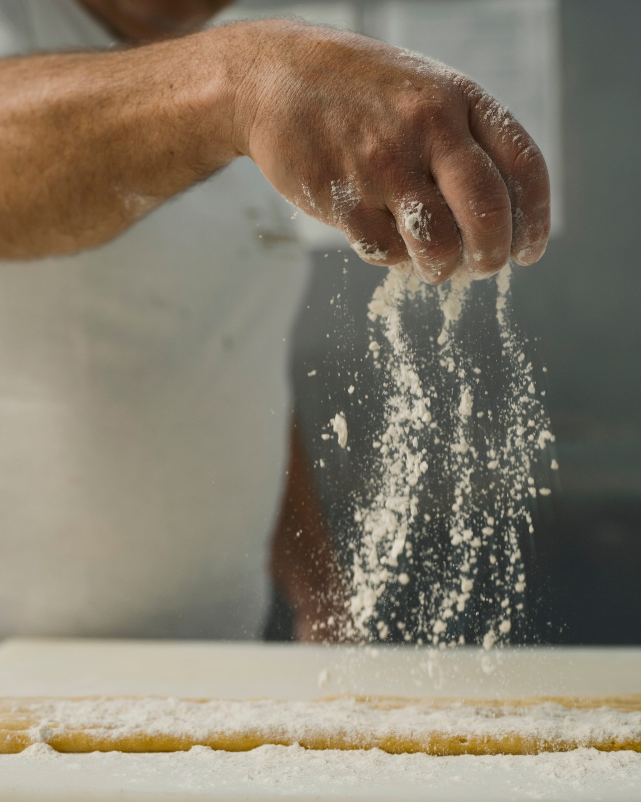 A baker's hand dusts flour over dough on a work surface.
