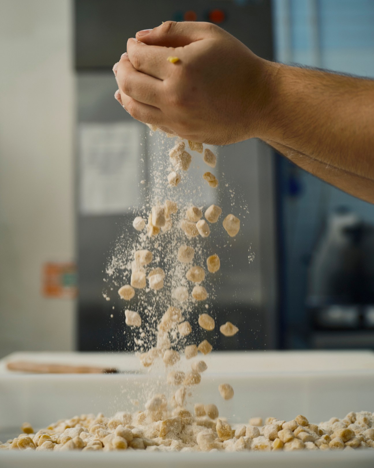 Hands dropping flour and dough pieces onto a floured surface in a professional bakery kitchen