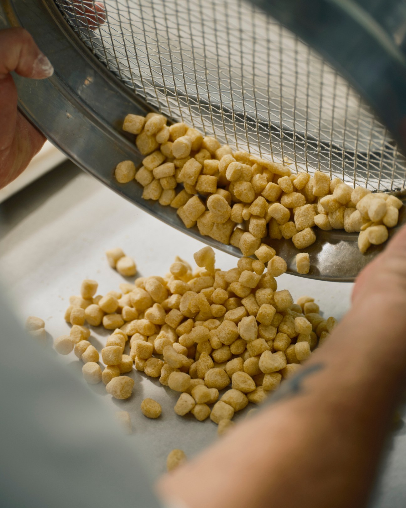 Golden Lebkuchen dough pieces being sifted through wire mesh basket onto white parchment paper
