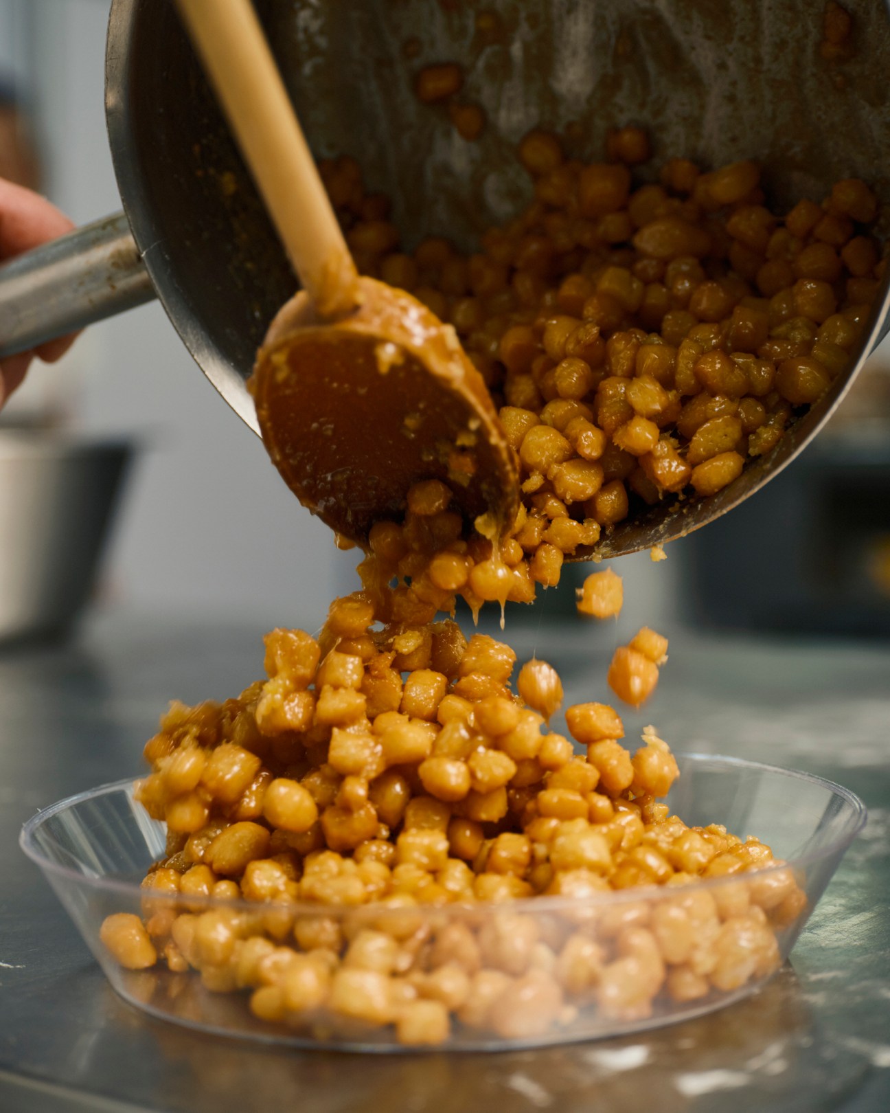 Golden caramelized nuts being poured from a ladle into a glass bowl, creating a glossy pile