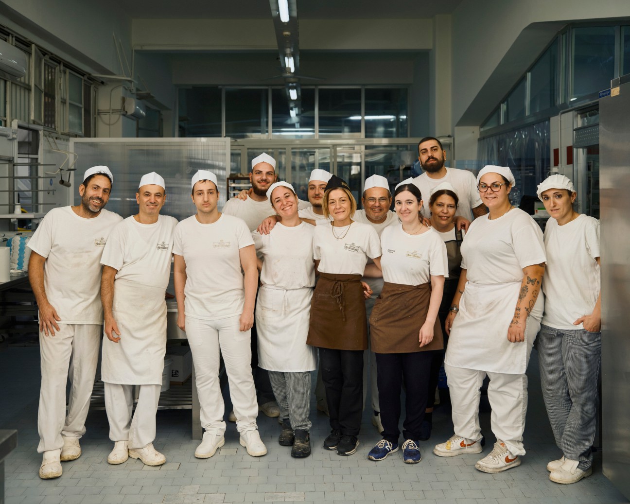 A team of bakers and pastry chefs in white uniforms and hats posing together in a professional kitchen