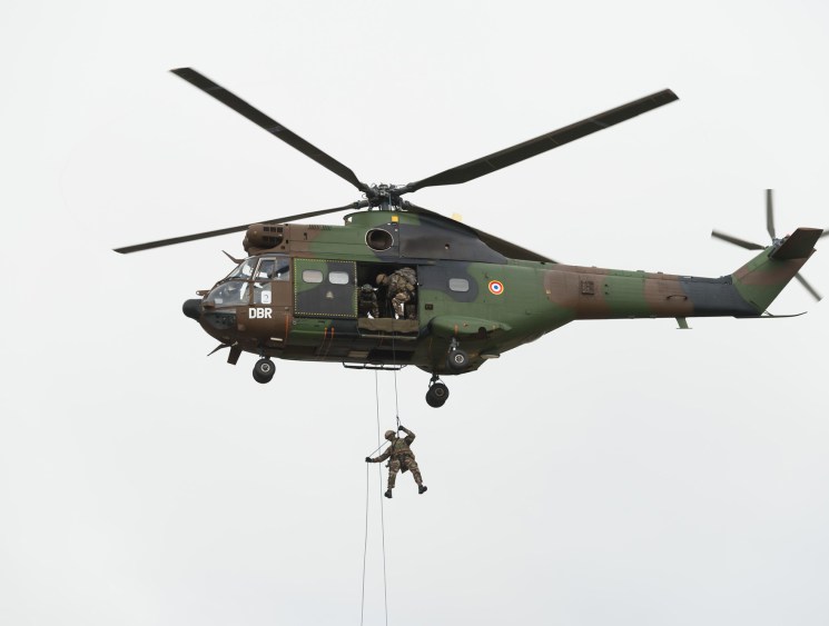 Army green helicopter with soldier being lowered.