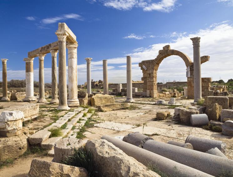 Ancient Roman ruins with stone columns, arches and scattered marble fragments under blue sky in Libya