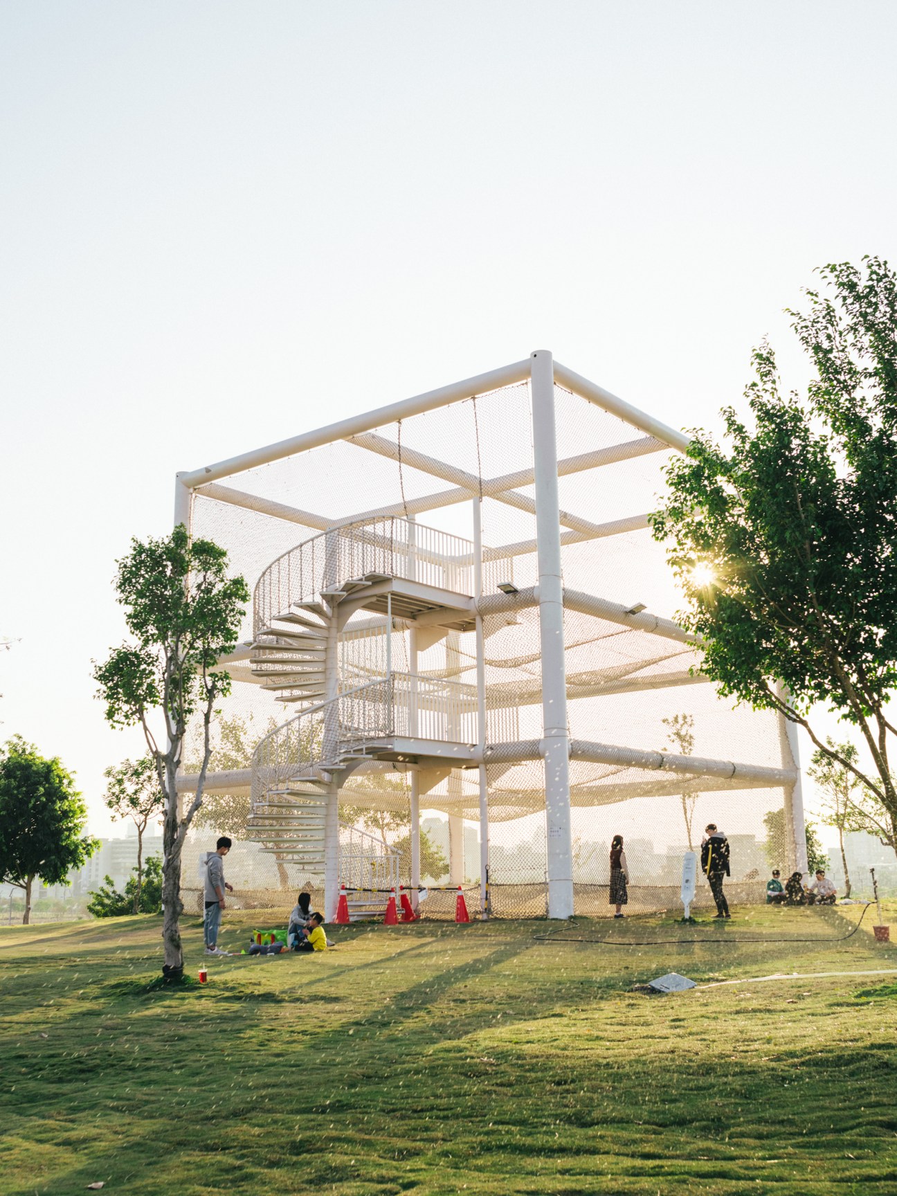 Modern multi-level observation tower with spiral staircase and viewing platforms surrounded by people on grass