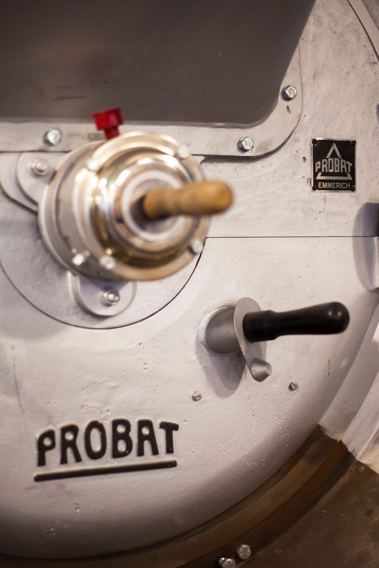 Close-up of a Probat Emmerich machine with metal components and wooden handle on white surface.