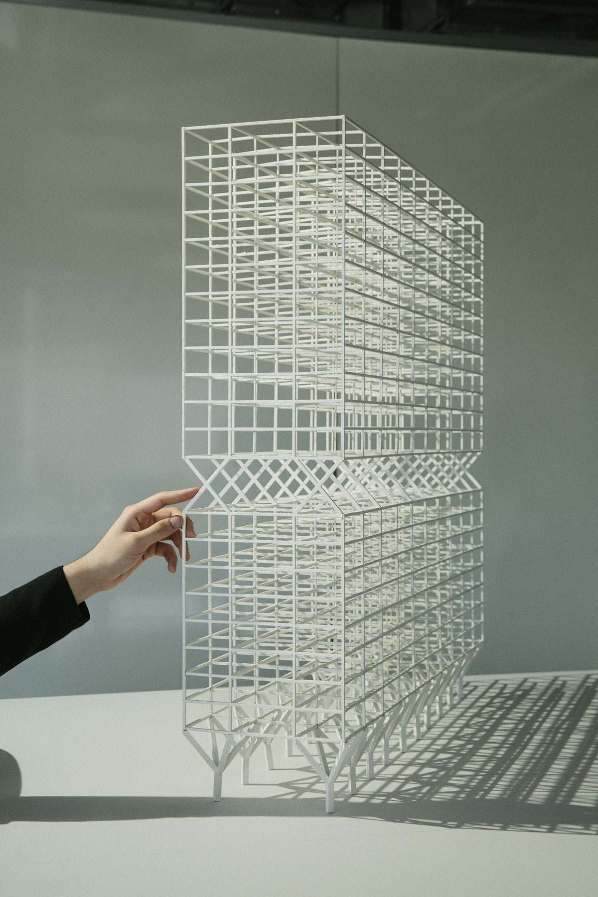 White skeletal architectural model showing grid-like framework structure with hand reaching toward it