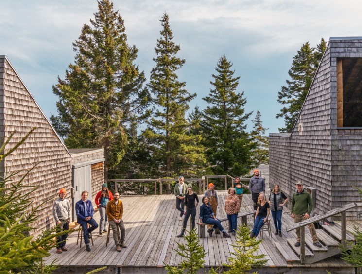 Team members of Haystack Mountain School of Crafts standing together on wooden deck surrounded by cedar buildings