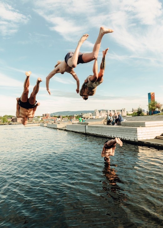 Young people diving and jumping from a wooden dock into water in Oslo