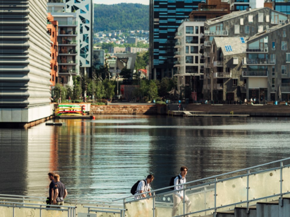 Modern waterfront buildings and pedestrian bridge in Oslo with people walking along the water