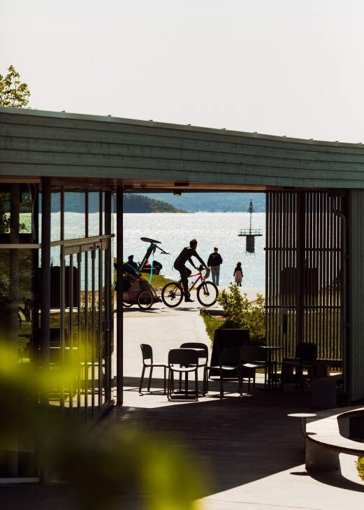 Modern pavilion structure with outdoor seating overlooking Oslo waterfront with cyclists and people enjoying the space