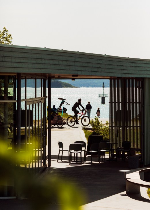 Modern pavilion structure with outdoor seating overlooking Oslo waterfront with cyclists and people enjoying the space