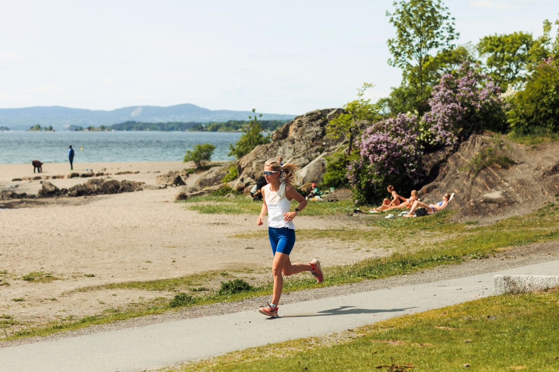 Runner jogging along coastal path with beach, water, and flowering trees in background