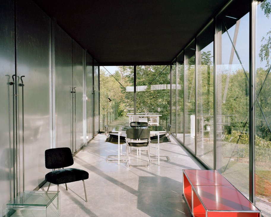 Modern glass house with floor-to-ceiling windows overlooking wooded landscape