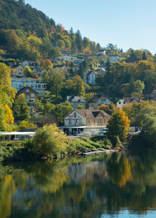 Besançon, France: A riverside town nestled in forested hills with historic buildings and a railway station reflected in the water.
