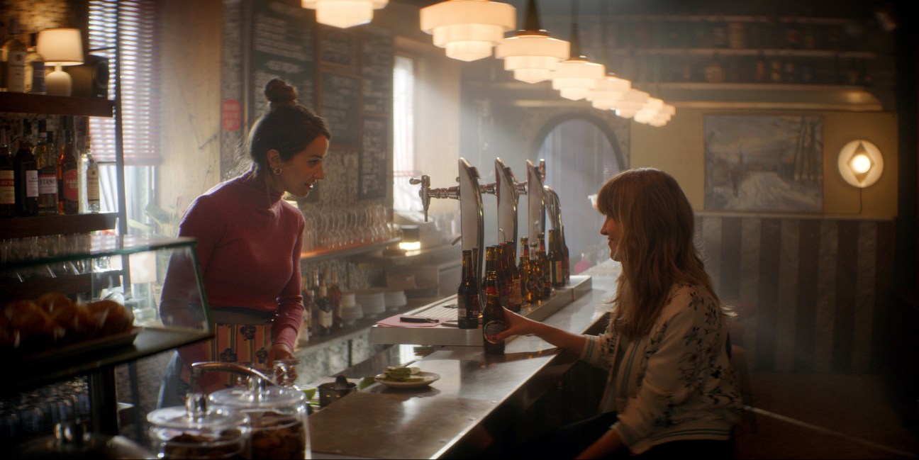 Two women sitting at a restaurant bar with pendant lighting overhead