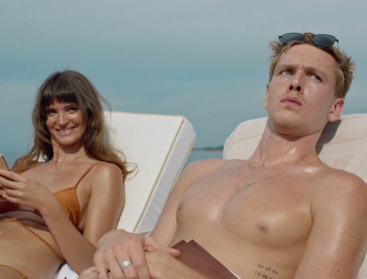 Two people lounging on deck chairs aboard a luxury yacht, woman in bikini using phone, shirtless man beside her