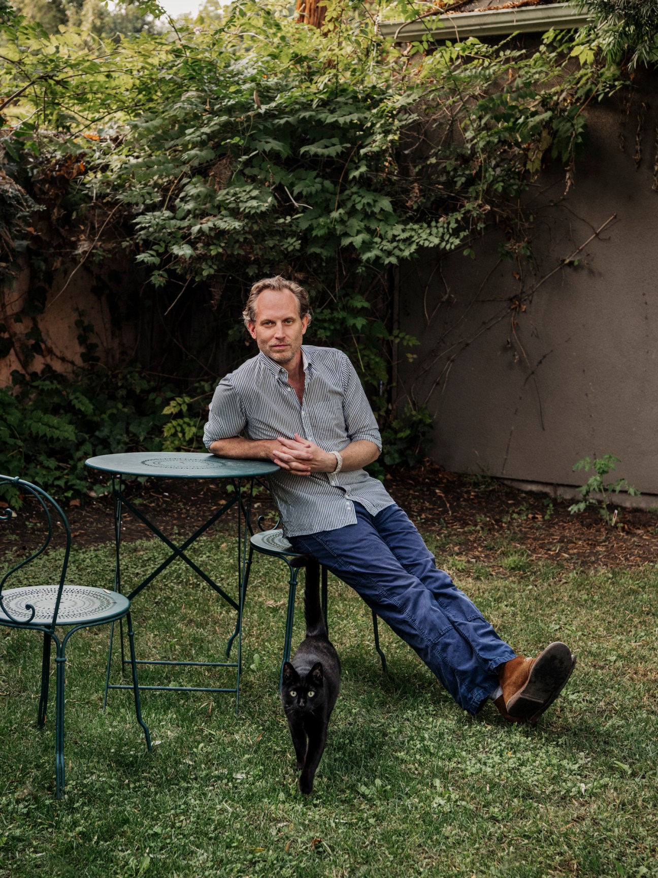 Portrait of Tyler Maroney, author and private detective, sitting at outdoor table with black cat