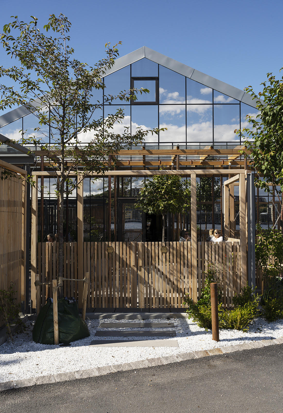 Modern glass and steel restaurant building with wooden veranda and pergola structure surrounded by trees