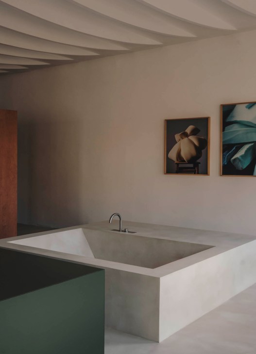 Modern bathroom with built-in white bathtub, curved ceiling beams, and framed artwork on neutral walls