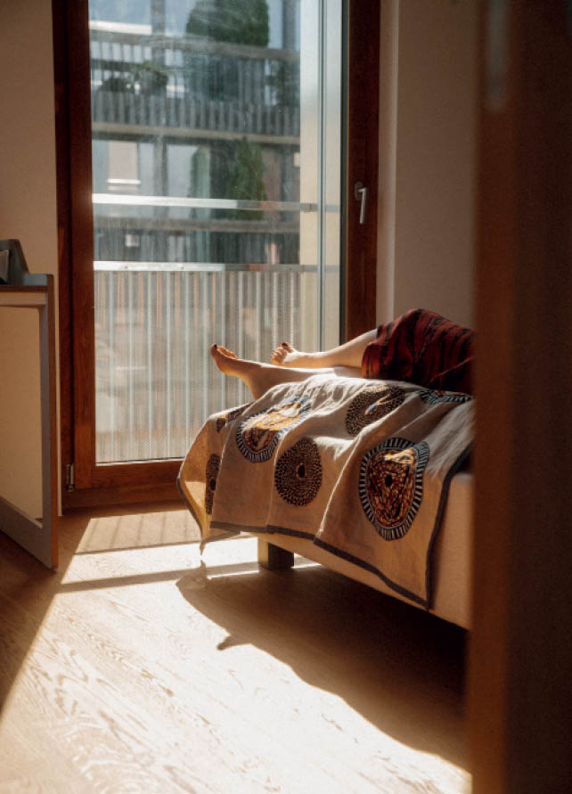Person lounging on a bed by a large window overlooking a Küsnacht apartment balcony and courtyard.