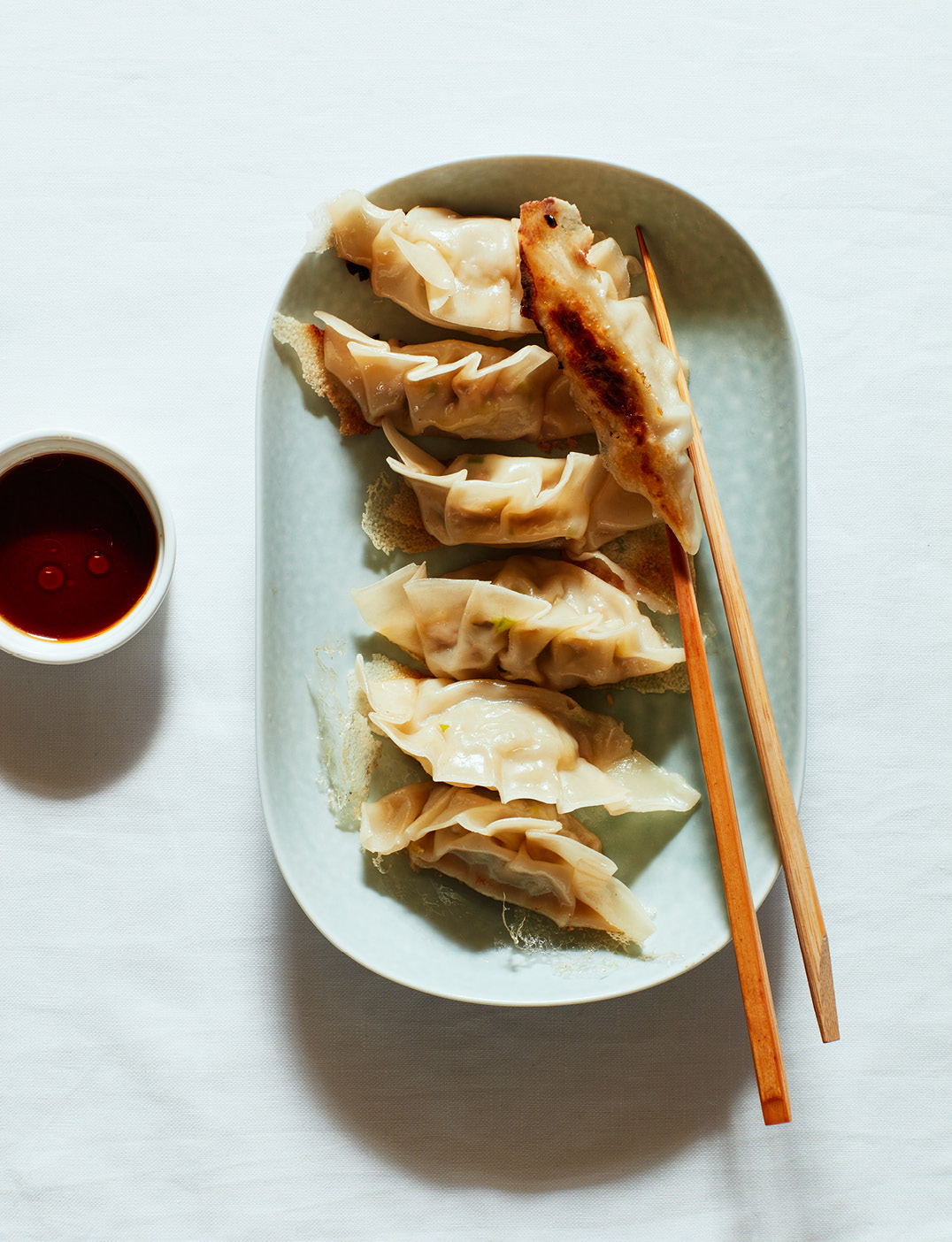 Six pan-fried pork gyoza dumplings arranged on a pale green rectangular plate with wooden chopsticks and a small bowl of dipping sauce.