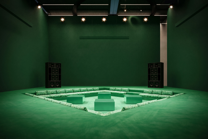 Green architectural installation with curved seating arrangement and decorative pillars in an indoor space
