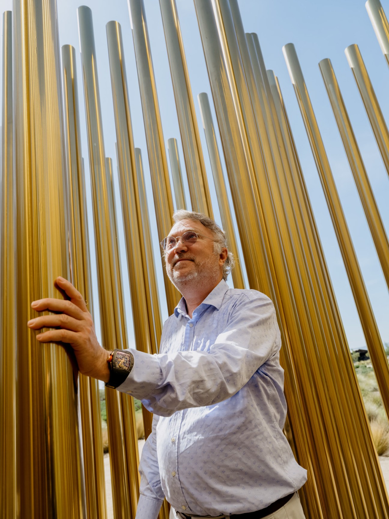 Man in light blue shirt touching golden metal pipes at sculpture installation