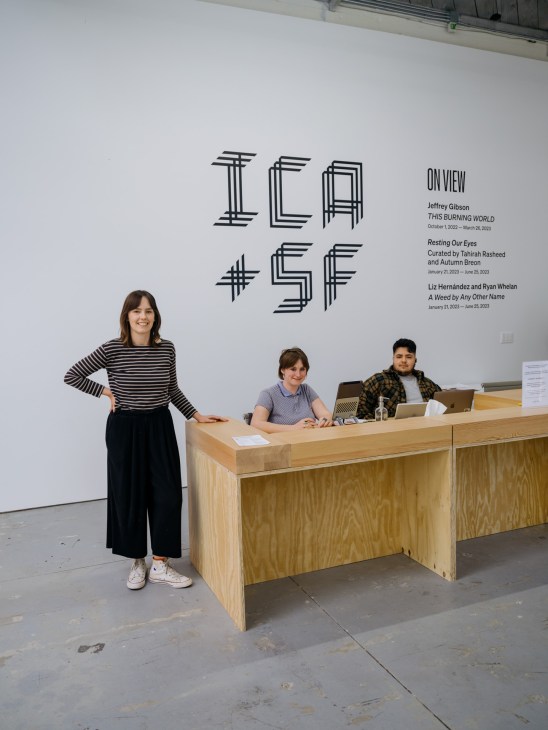 Three staff members at ICA San Francisco reception desk with gallery wall signage visible behind