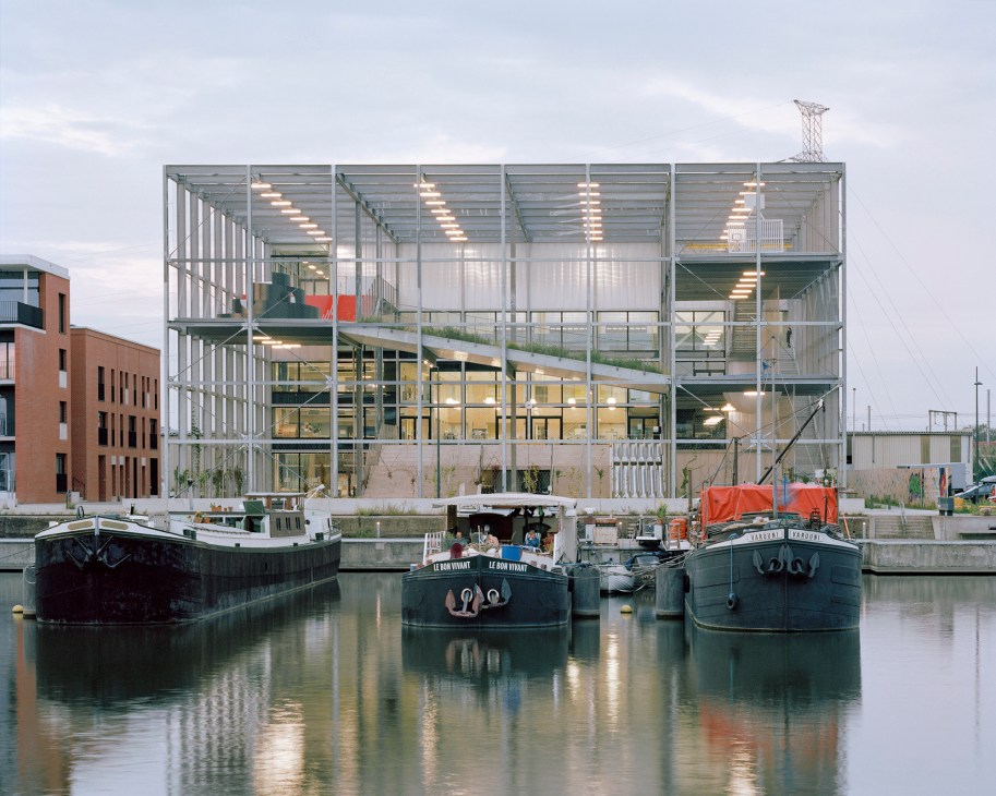 Melopee school in Ghent with transparent steel grid structure overlooking waterfront and landscape.