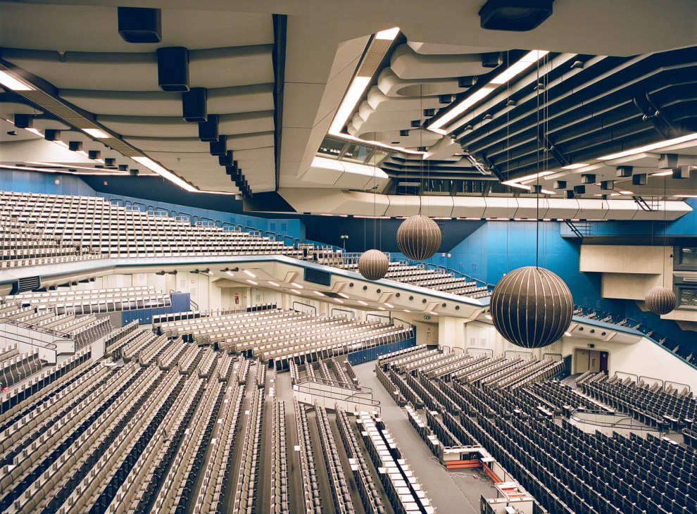 Interior of Saal 1, the 5,000-seat auditorium at Berlin's International Congress Centre, showing rows of seats, blue walls, and spherical speakers hanging from the ceiling.