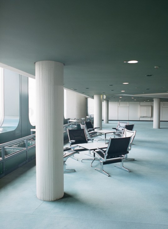 Modern conference room interior with black leather chairs, white columns, and turquoise ceiling at ICC Berlin.