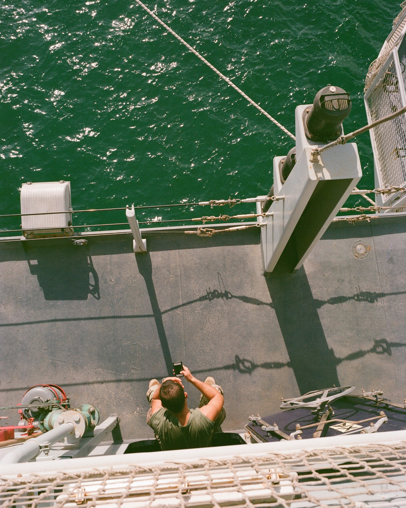 Sailor adjusting headwear while working on the Cavour aircraft carrier deck overlooking green ocean water.