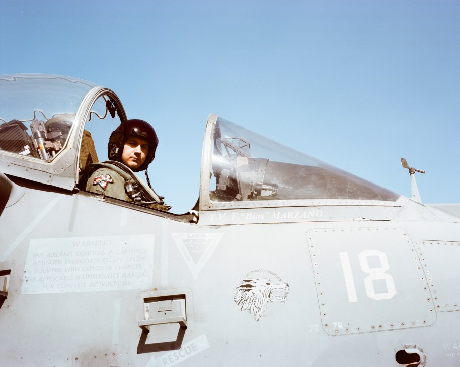 Fighter pilot Fabio 'Bias' Marzano in cockpit of AV-8B Harrier II jet with helmet and flight suit.