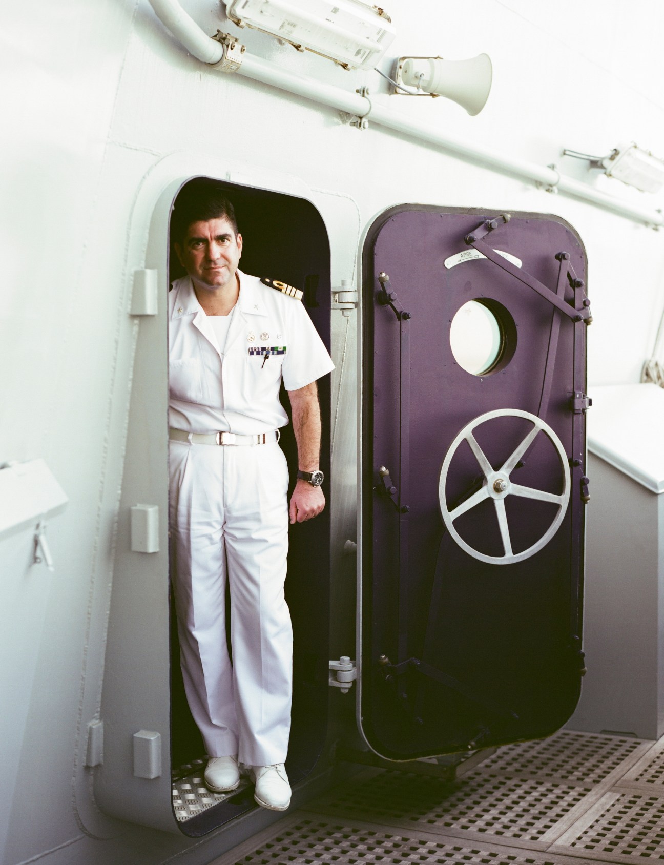 Captain Francesco Milazzo in white naval uniform standing in a doorway aboard the Cavour aircraft carrier.