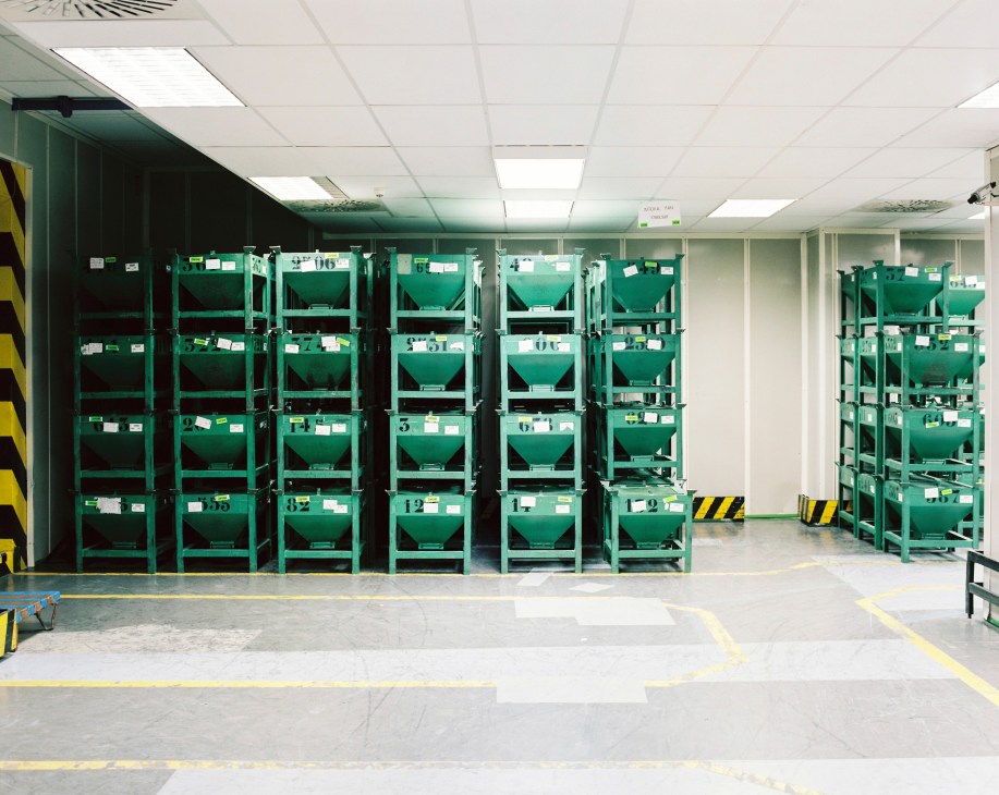 Green metal storage bins filled with packaged currency in an industrial warehouse facility.