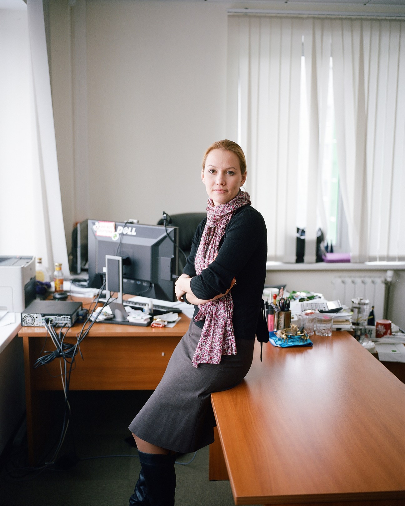 Woman in black blazer and patterned scarf posing at desk with computer monitor