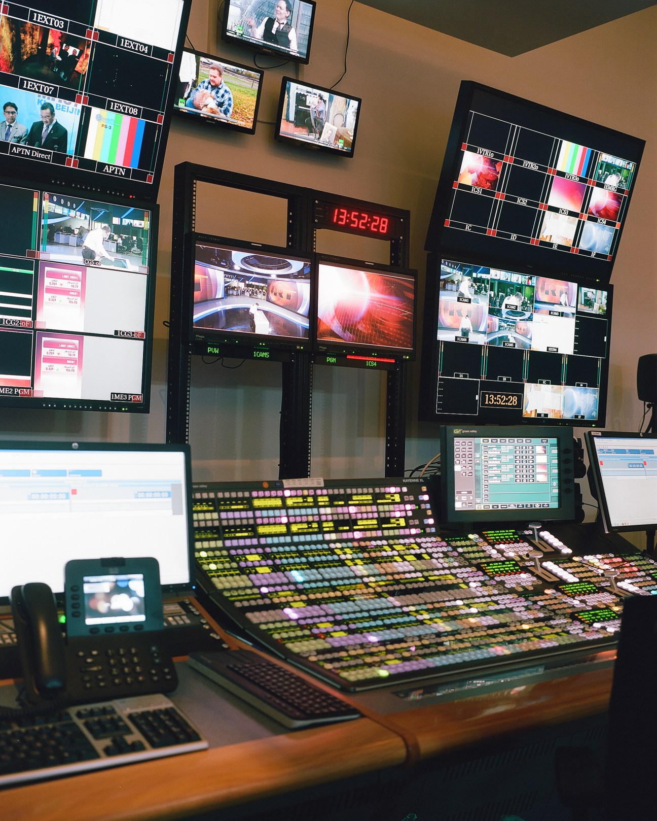 Broadcasting control room with multiple monitors displaying news feeds, a colorful mixing console, and technical equipment.