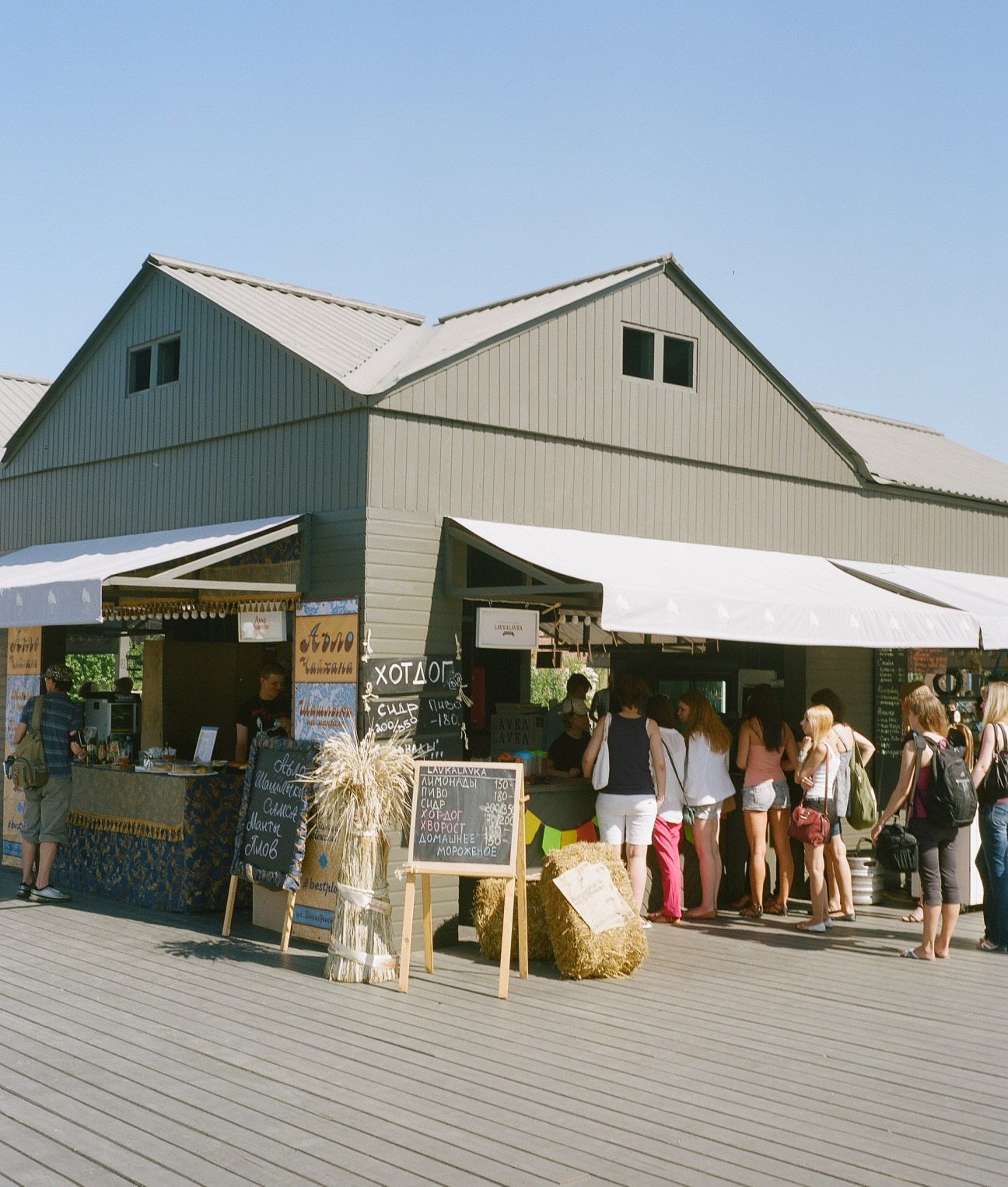 Food stalls and vendors at New Holland market with people queuing under white awnings and green corrugated metal structures.
