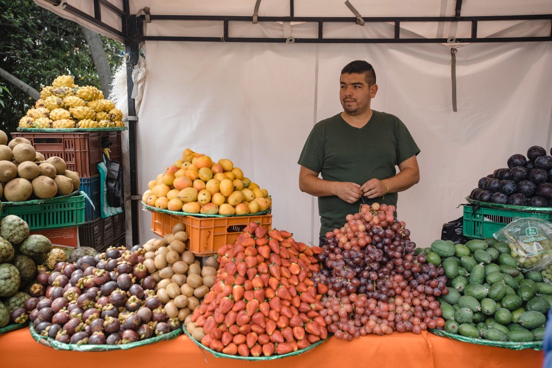 A fruit vendor stands behind colorful displays of tropical produce at Usaquén market.
