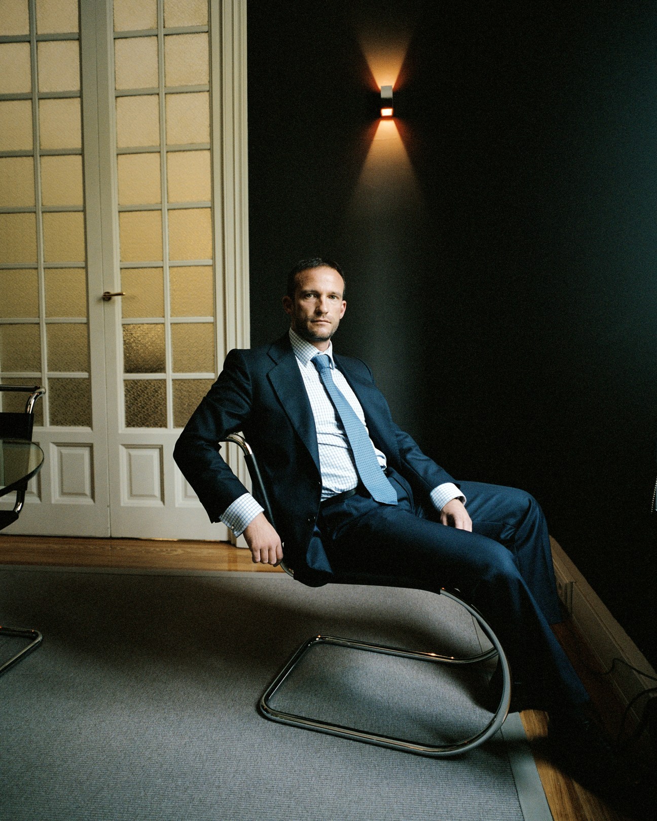 Man in navy suit and blue tie sitting in modern office with gridded window
