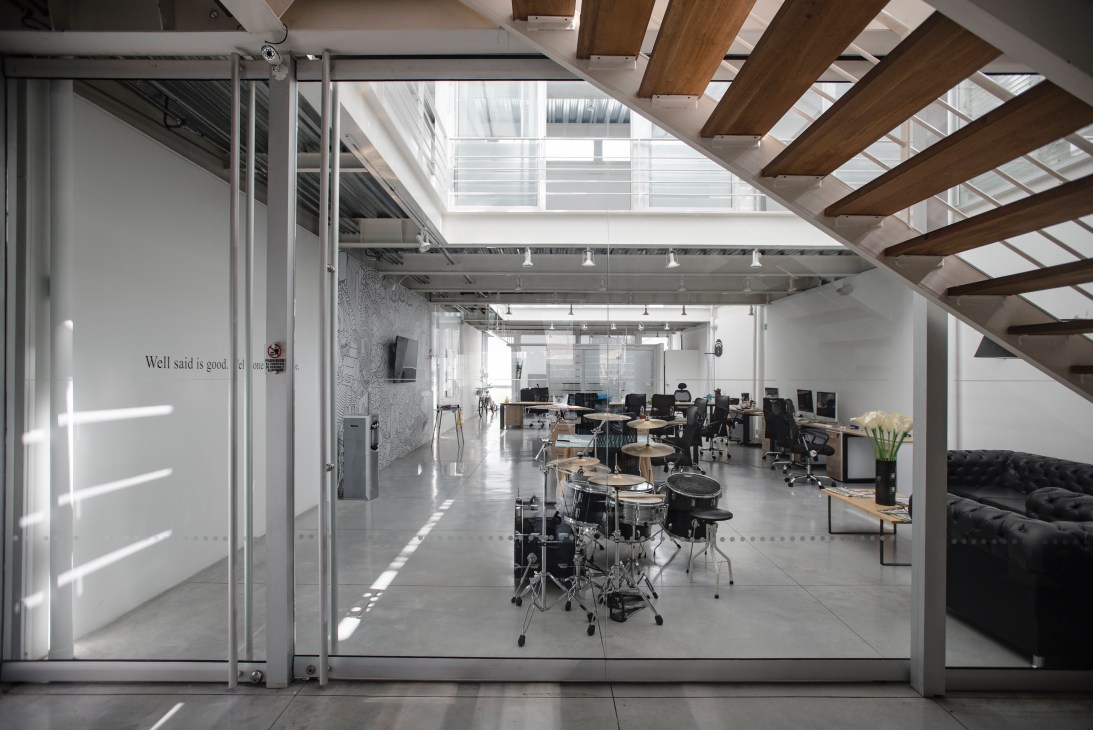 Modern ad agency office with open-plan workspace, drum kit, wooden ceiling beams, and glass partitions.