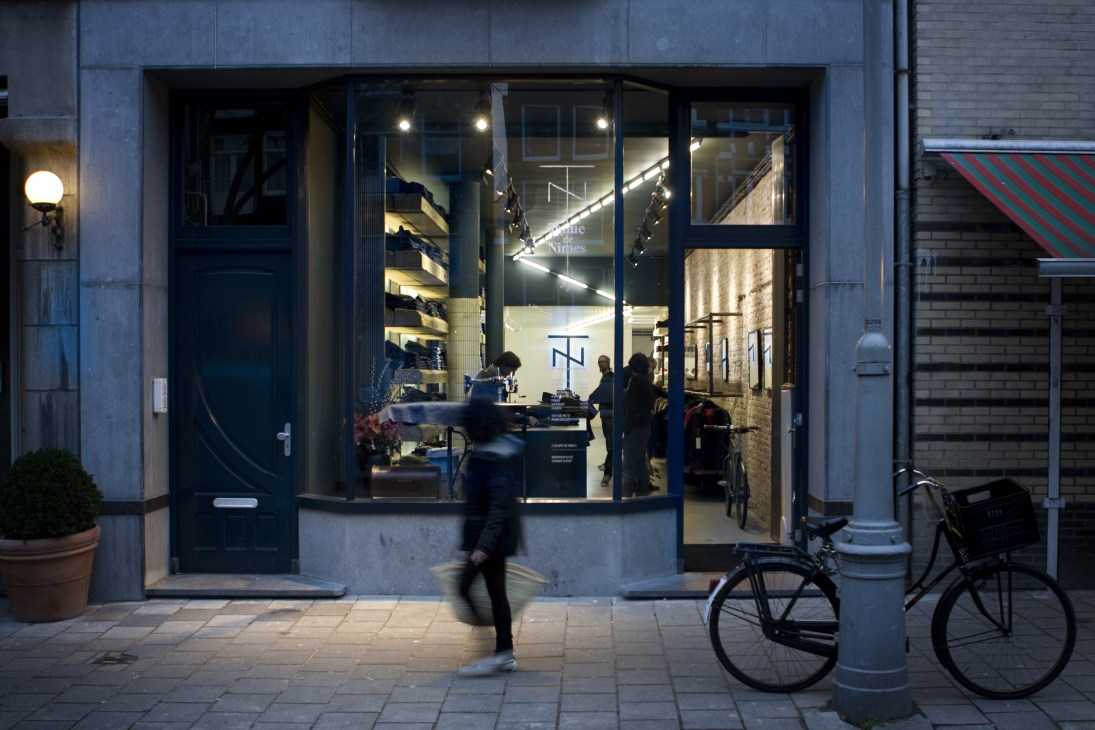 Slowear storefront on a quiet Paris street at dusk with large windows, interior lighting, and a bicycle parked outside.