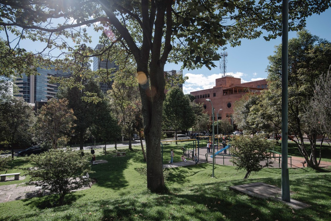 Tree-shaded park with playground, brick buildings and modern high-rises visible beyond the greenery in Bogotá.